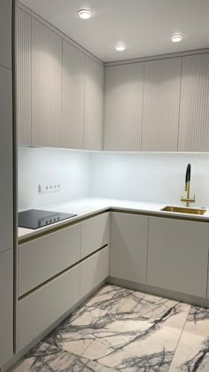 a kitchen with marble flooring and white cabinets in the corner, next to a gold faucet