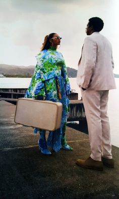 a man and woman standing next to each other near the water with their suitcases