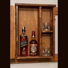 two bottles of liquor are sitting in a wooden box with glasses on the shelf next to it