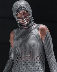 a woman in silver is wearing a metal outfit with chains on her face and chest