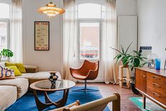 a living room filled with furniture next to two windows and a blue rug on top of a hard wood floor