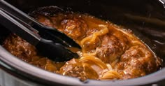 a slow cooker filled with meatballs and cheese being stirred by two tongs