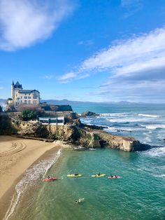 people are kayaking in the ocean near a castle on top of a cliff overlooking the beach