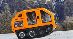 an orange and black vehicle on snow covered ground with mountains in the backgroud