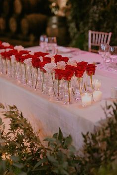 a long table with candles and red roses in vases on it's side