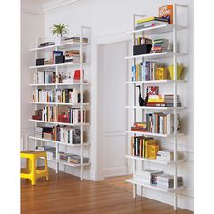 a white book shelf filled with books on top of a hard wood floor next to a yellow chair