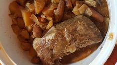 a white bowl filled with meat, potatoes and carrots on top of a table