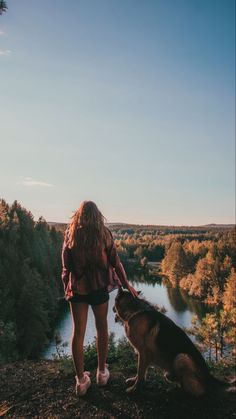 a woman standing next to a brown dog on top of a hill near a river