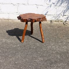 a wooden stool sitting on top of a cement ground next to a white brick wall