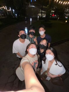 a group of people wearing face masks taking a selfie with their cell phones at night