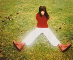 a woman sitting in the grass with her legs crossed and wearing white pants, red shoes