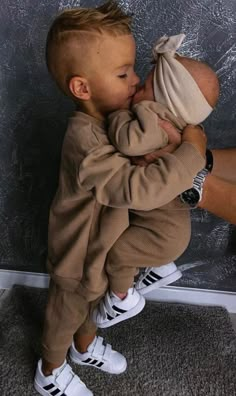 a young boy is kissing his mother's face while she sits on the floor