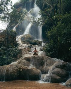 a person sitting on top of a rock in front of a waterfall