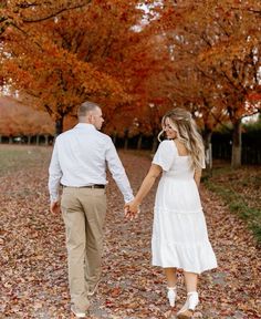 a man and woman holding hands while walking through leaves