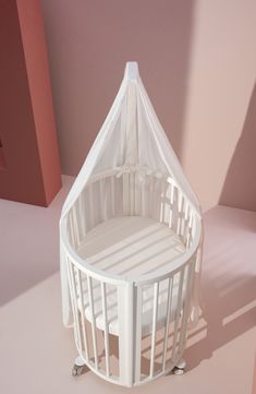 a white baby crib sitting on top of a pink floor next to a wall