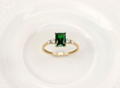 an emerald colored ring with three diamonds on the side, sitting on a white plate