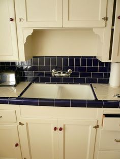 a kitchen with blue and white tiles on the counter top, sink and cupboards