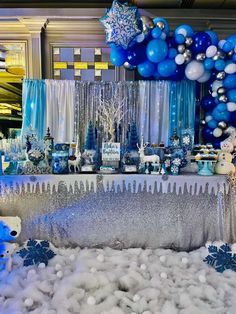 a blue and white dessert table with balloons, snowflakes, and other decorations