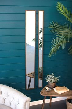 a mirror sitting on top of a wooden table next to a white chair and potted plant