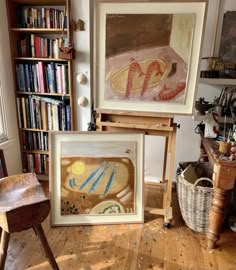 two paintings on easels in front of a bookshelf