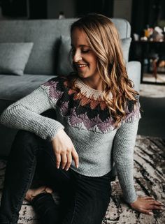 a woman sitting on the floor in front of a gray couch smiling at someone else