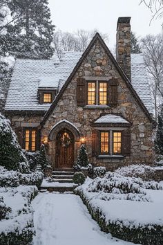 a house covered in snow and surrounded by hedges with lights on the front door,