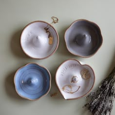 four ceramic bowls are shown next to some dried flowers and a small gold necklace on the bottom