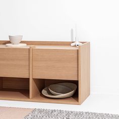 a wooden cabinet with two bowls on it and one bowl in the middle, next to a white wall