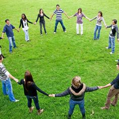 a group of people holding hands in the middle of a circle on grass with trees in the background