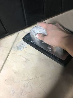 a person with a rag on their hand cleaning a tile floor in front of a black cabinet