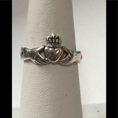 a silver cladder's ring with a crown on the front and sides, sitting on top of a white pedestal