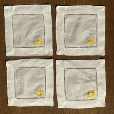 four napkins with embroidered lemons on them sitting on top of a wooden table