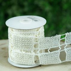 a spool of white crochet ribbon sitting on top of a wooden table