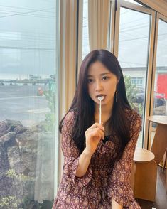 a woman sitting in front of a window holding a toothbrush