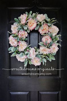 a wreath with pink flowers and greenery hanging on the front door to welcome guests