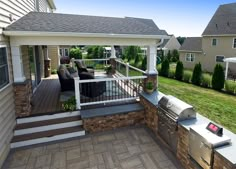 an outdoor kitchen with grill and seating on the back deck in front of a house