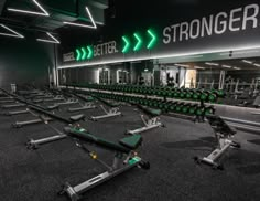 an empty gym with rows of weight benches and green neon signs on the wall behind them