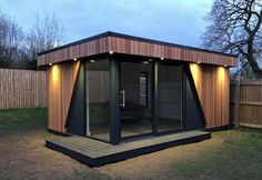 a small wooden building with sliding glass doors and lights on the outside, next to a fence