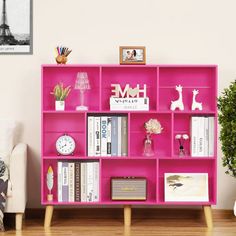 a pink bookcase with books and pictures on it next to a potted plant