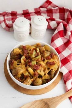 a white bowl filled with pasta and meat on top of a wooden cutting board next to two salt shakers