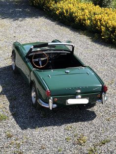 an old green sports car parked on gravel