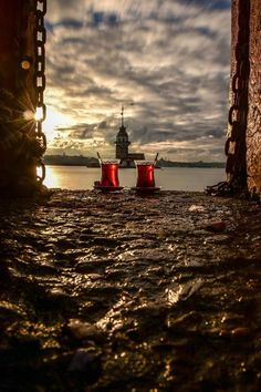 two red fire hydrants sitting in the middle of a body of water with a lighthouse in the background