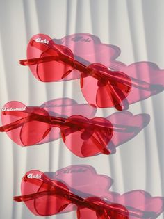 three pairs of heart shaped sunglasses sitting on top of a white surface with red tinted lenses