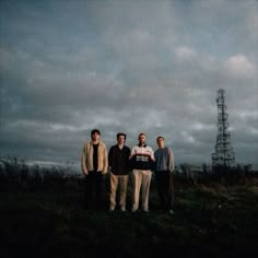 four men standing in the grass under a cloudy sky