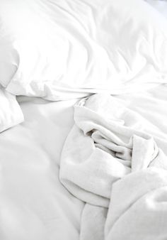 an unmade bed with white sheets and pillows