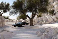 a black car parked in front of a tree on top of a rock covered hillside