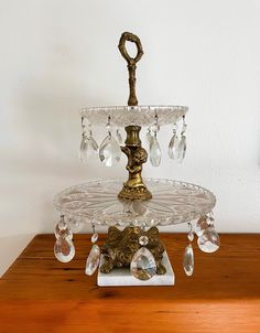 a three tiered glass cake stand with crystal beads and a golden candle holder on top