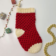 a red and white crocheted christmas stocking next to a beaded ornament