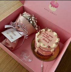 a birthday cake in a pink box with flowers on the side and a card inside