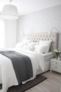 a bed with white linens and pillows in a bedroom next to a lamp on a table